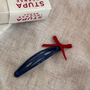 Détail d'une barrette bleu foncé avec un petit nœud en ruban rouge sur tissu beige