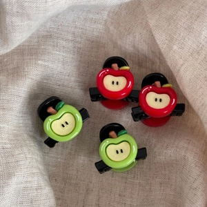 Close-up of mini red and green apple hair clips on a textured linen background