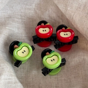 Set of four cute red and green 3D apple-shaped hair mini claws on a textured beige background