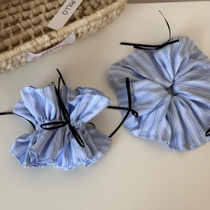 Detail of two blue striped scrunchies with black ribbon bows on a beige surface