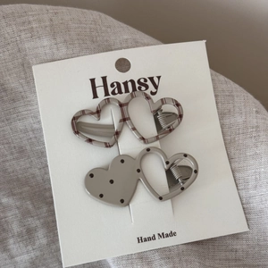 Detail of two heart-shaped hair clips with plaid and polka dot patterns on display card
