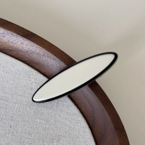 Détail macro d'une pince à cheveux crème avec lignes noires sur un plateau en bois sombre