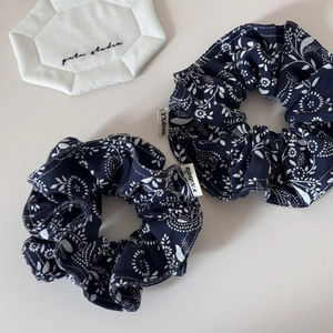 Detail view of two navy floral scrunchies with white paisley patterns and brand labels