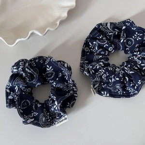 Detail of two navy floral cotton scrunchies with white petal patterns and logo label