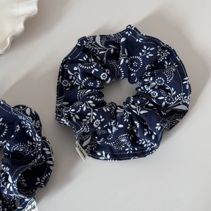 Set of two navy blue floral scrunchies with white leaf print on a minimalist surface