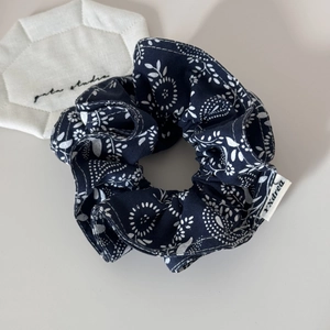 Detailed close-up of a navy blue floral scrunchie with white flower patterns and woven tag