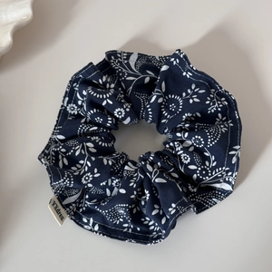 Detail of navy blue floral scrunchie with white flower print and woven brand tag