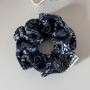 Detailed macro view of navy blue floral scrunchie with white botanical pattern and label