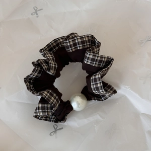Detail of checkered plaid and brown fabric scrunchie with a large central pearl accent
