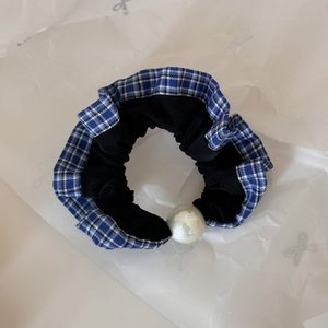 Detail view of plaid lace hair scrunchie with a large pearl on white wrinkled paper