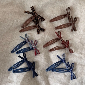 Vue à plat de 6 paires de barrettes à nœuds colorés aux motifs variés sur toile de jute