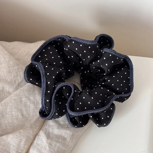 Detail showing black polka dot hair scrunchie with blue stitched edges on linen fabric