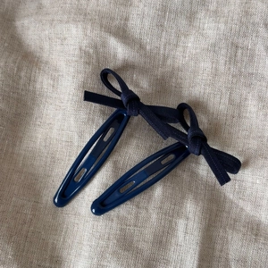 Gros plan de deux barrettes à nœuds bleu marine sur un fond en lin beige naturel