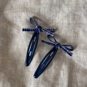 Détail de deux barrettes à cheveux à nœud vichy bleu et blanc sur fond de lin rustique