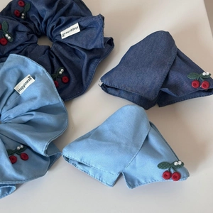 Detailed view of denim hair scrunchies with red cherry embroidery and Happiness label