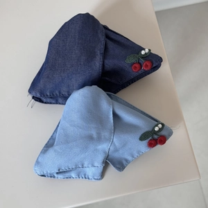 Detailed close-up of denim bow clips with cherry embroidery and white pearl accents