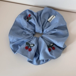 Detail of blue cotton scrunchie with red cherry embroidery, white pearls and logo label