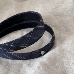 Close-up of a navy plaid fabric headband with a small silver heart-shaped charm