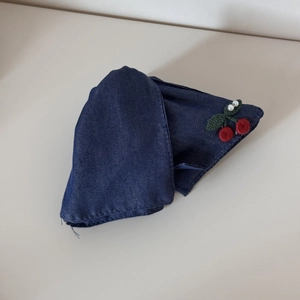Detailed view of dark blue denim fabric with red cherry embroidery and white pearls