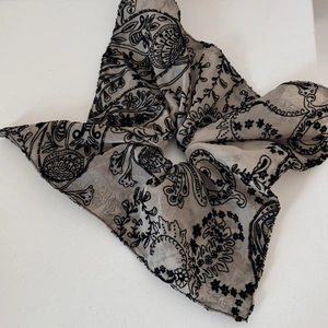 Close-up of beige chiffon scrunchie with black paisley floral pattern and bow detail