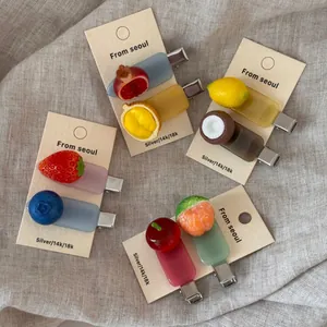 Detailed view of fruit-shaped acetate hair clips on beige linen texture background