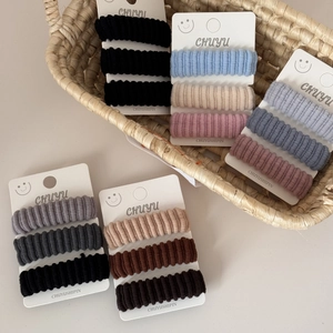 Detailed close-up of three high-elasticity ribbed hair ties in a woven grass basket