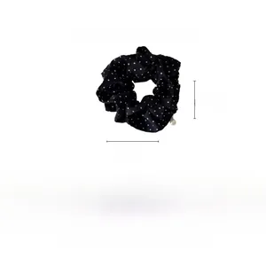 Detail showing a black polka dot fabric scrunchie with pearl charm measuring 12x12cm