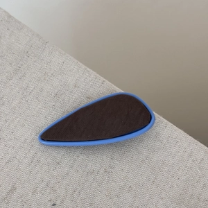Gros plan d'une barrette rétro bleu et marron contrastée sur un tissu texturé gris