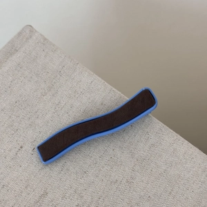 Détail de la pince à cheveux ondulée bleu denim et marron sur un fond texturé beige clair