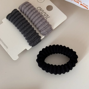 Detailed view of three elastic hair scrunchies in gray and black on brand card