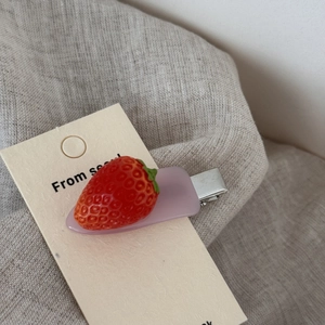 Detailed macro view of realistic red strawberry acetate hair clip on display card