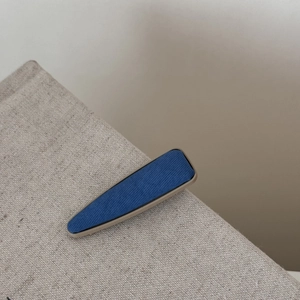 Vue détaillée d'une barrette à cheveux en denim bleu et kaki sur fond de lin brut