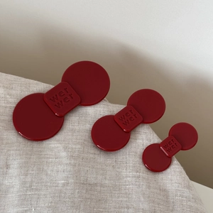 Close-up of three dark red acetate hair clips with brand engraving on soft beige linen fabric