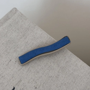 Détail d'une pince à cheveux ondulée bleu denim et marron sur fond de lin rustique