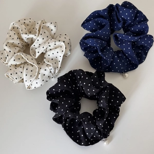 Close-up of three polka dot fabric scrunchies in black, navy and white with pearl charms