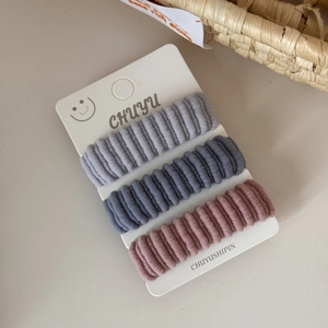 Detailed close-up of three ribbed fabric hair ties on display card in beige setting