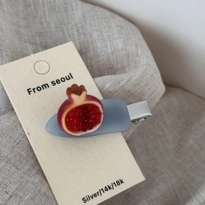 Close-up of a realistic pomegranate hair clip on a paper display card with linen background