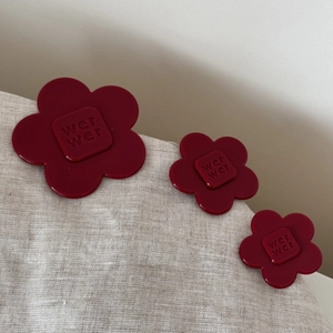 Detail of three wine red floral hair clips with embossed letters on a beige linen background