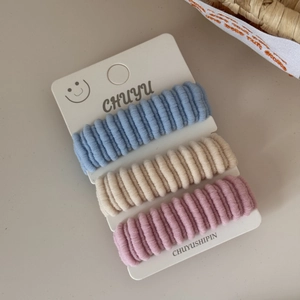 Detailed view of three elastic ribbed hair bands in blue, beige, and soft pink on a card