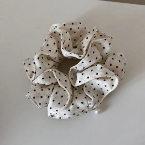 Detail of white polka dot scrunchie with silk texture and elegant pearl pendant accent