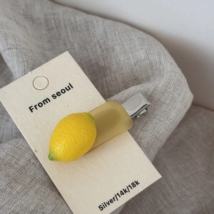 Detailed close-up of a realistic lemon acetate hair clip on a cream display card