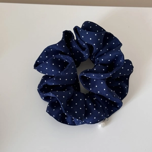 Close-up of a navy polka dot scrunchie with a white pearl charm on a plain background