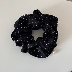 Detail of black polka dot scrunchie fabric with elegant white pearl pendant charm