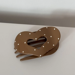 Detailed view of the brown polka dot heart shaped acrylic hair clip flat on the desk