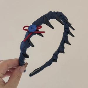 Dettaglio di cerchietto blu scuro con fiocco rosso, bottone blu e denti interni antiscivolo