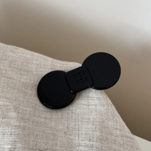 Detail shot of black acetate bow hair clip with engraved lettering on smooth surface