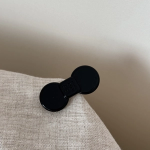 Detail of a black acetate bow hair clip with engraved lettering on a beige fabric edge