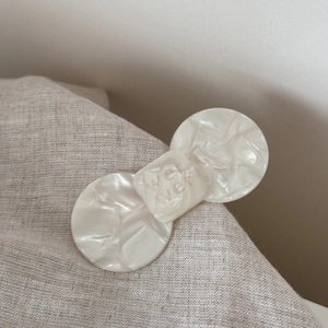 Macro detail of white acetate bow hair clip with embossed lettering on linen fabric
