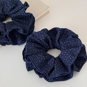 Detail of two navy blue scrunchies with light blue polka dots on a minimalist background
