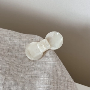 Close-up of cream acetate bow hair clip with engraved letters on linen fabric